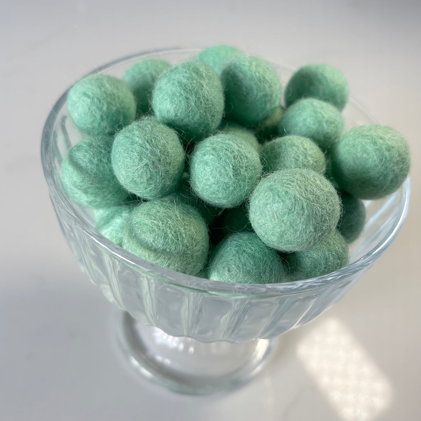 Glass bowl filled with aquamarine felt balls on a white background
