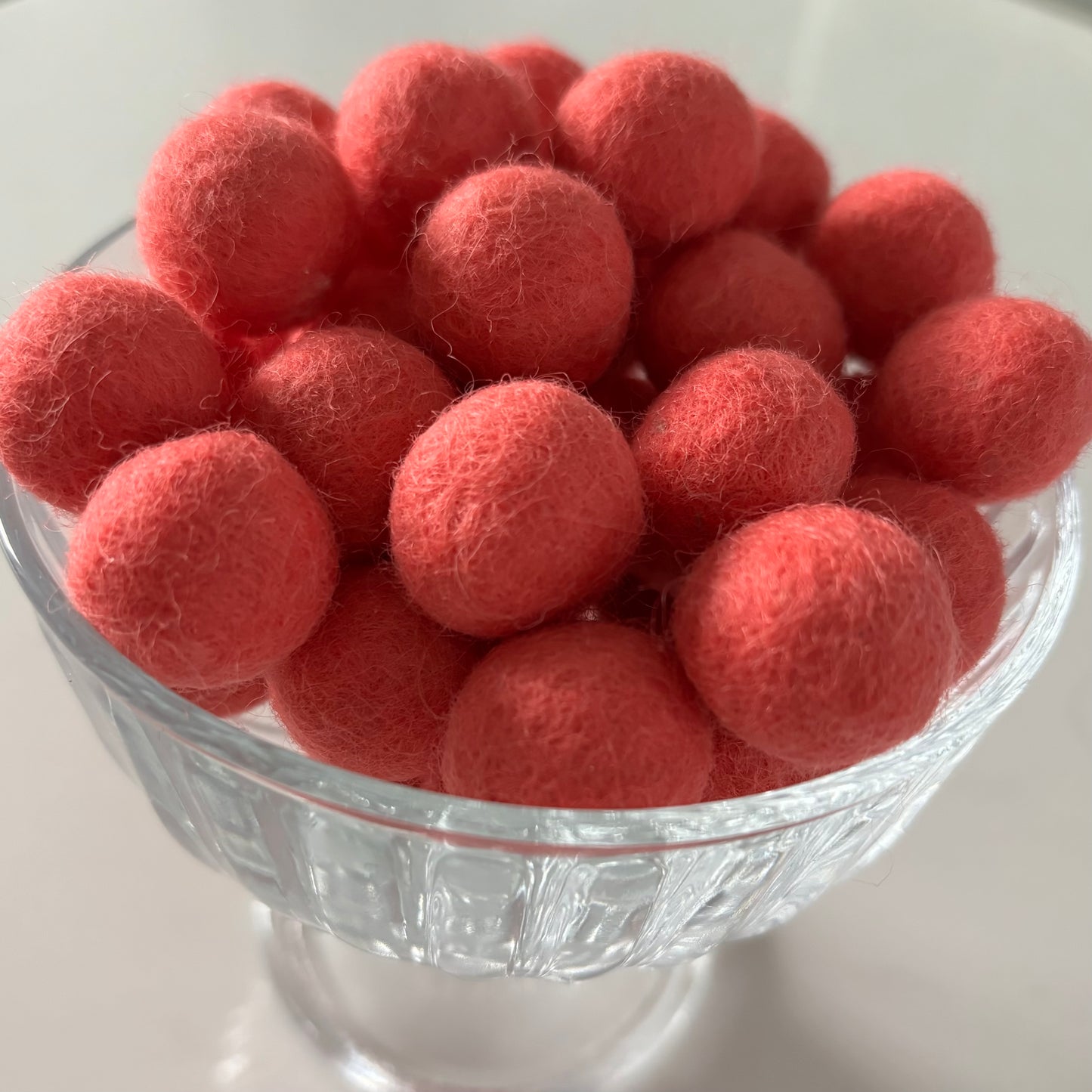 Coral felt balls in a glass bowl on a white background