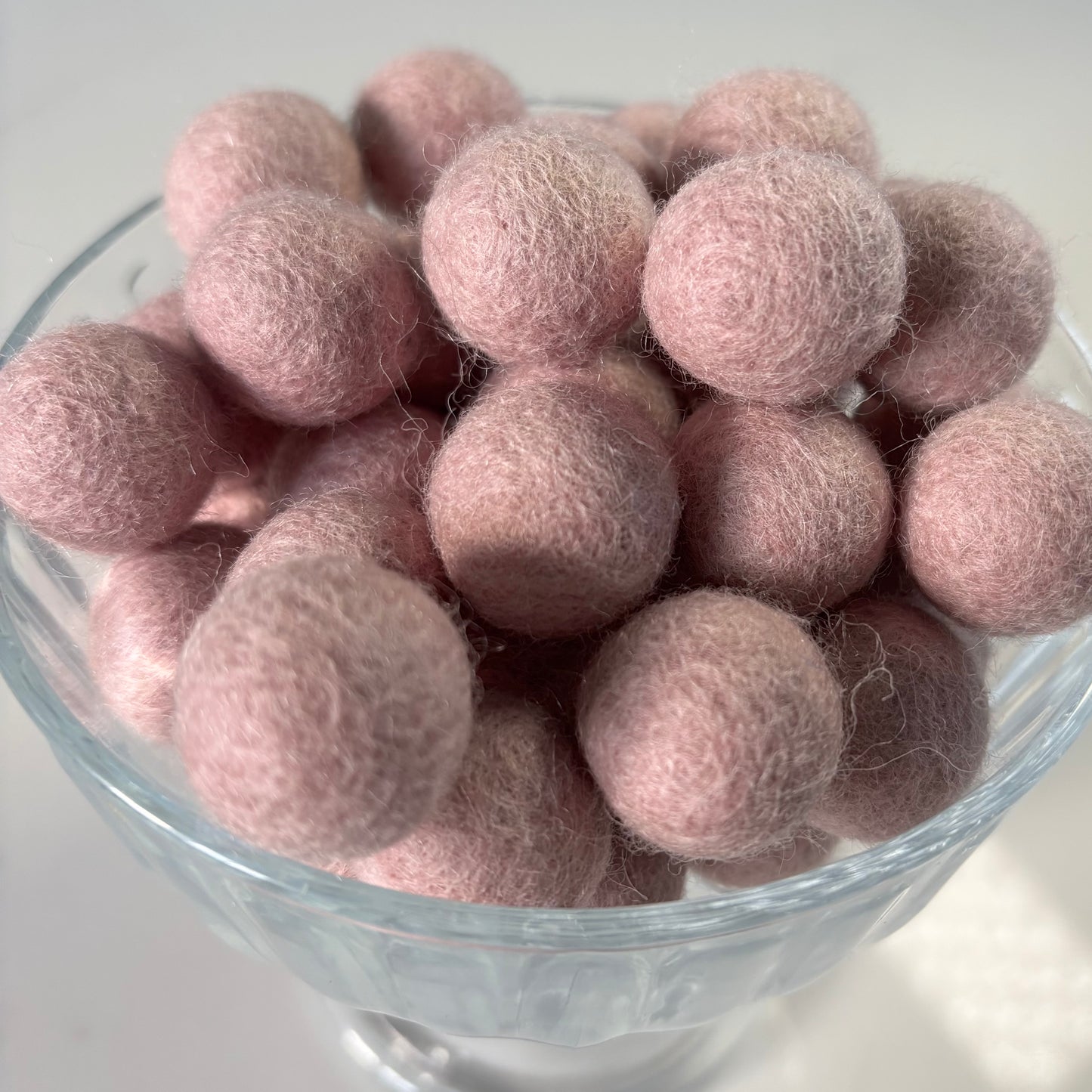 Glass bowl with pale pink felt balls ion a white background