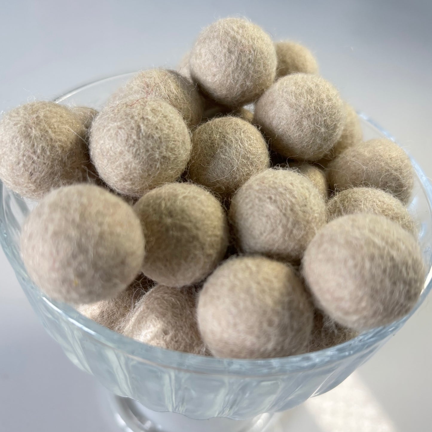 Glass bowl filled with beige felt balls on a light gray background