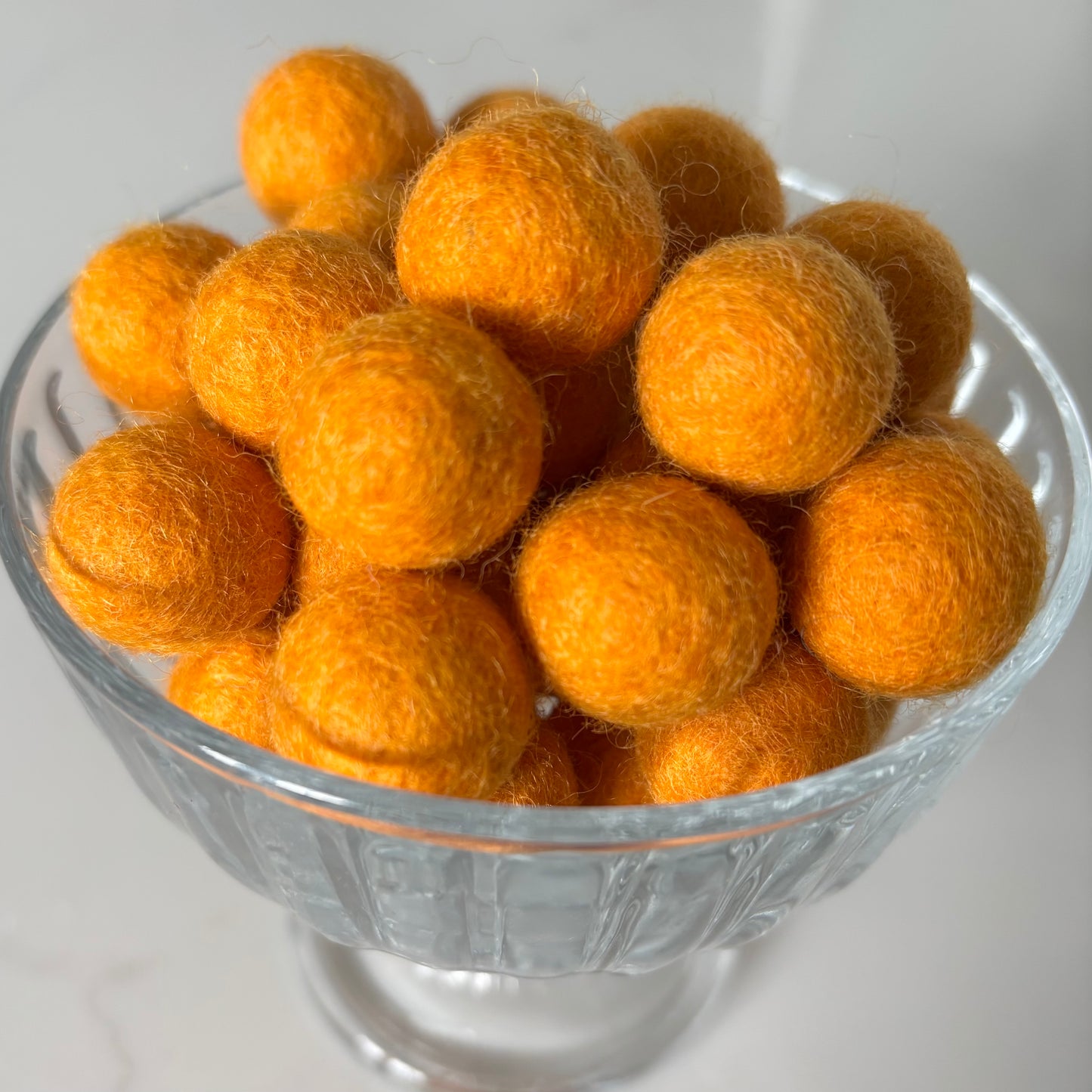 Clear glass bowl filled with orange felt balls on a white background