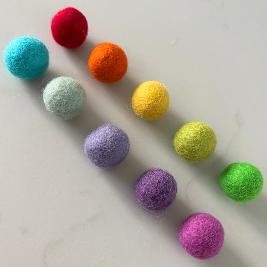 Colorful felt balls arranged in a scattered pattern on a light gray background