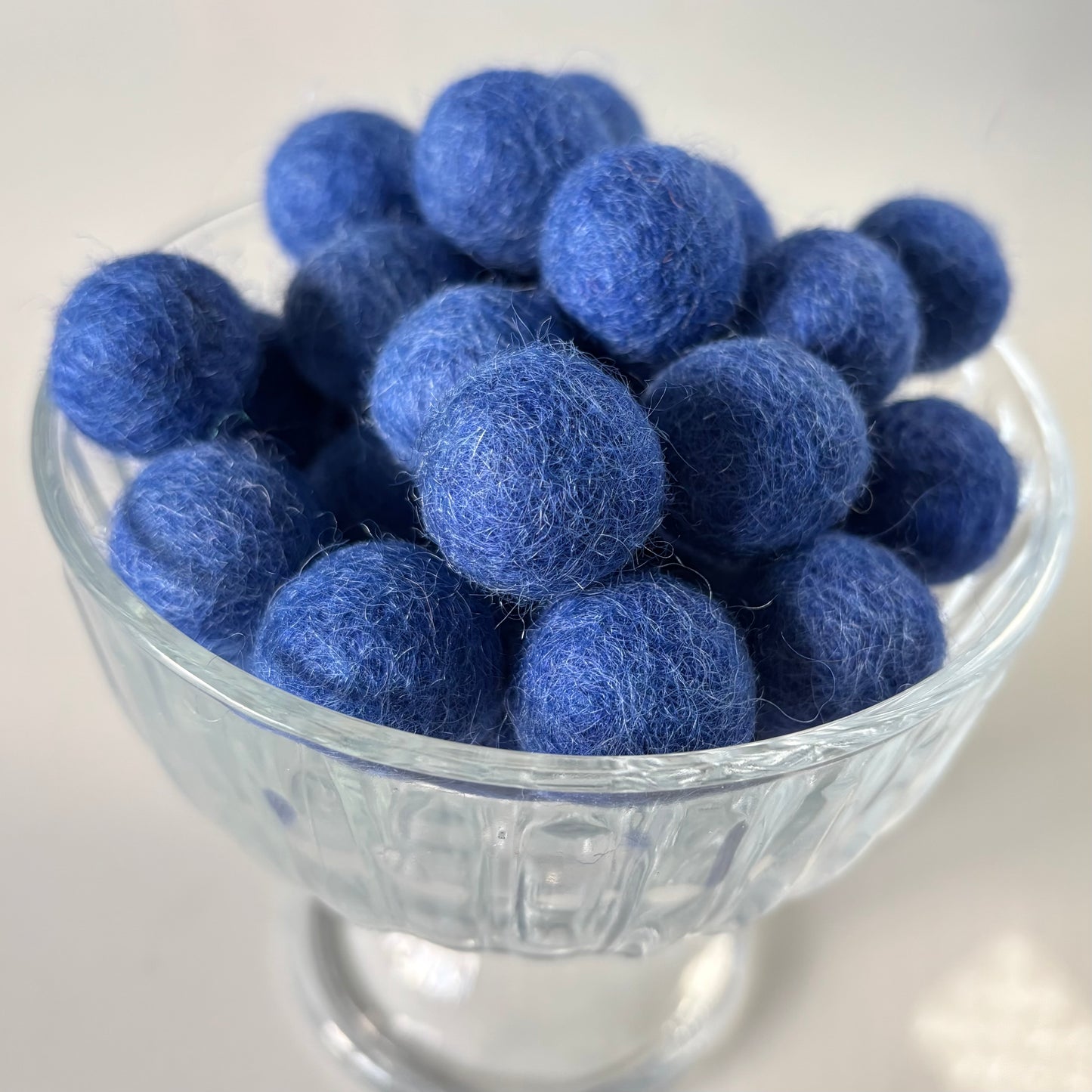 Royal blue felt balls in a glass bowl on a light background