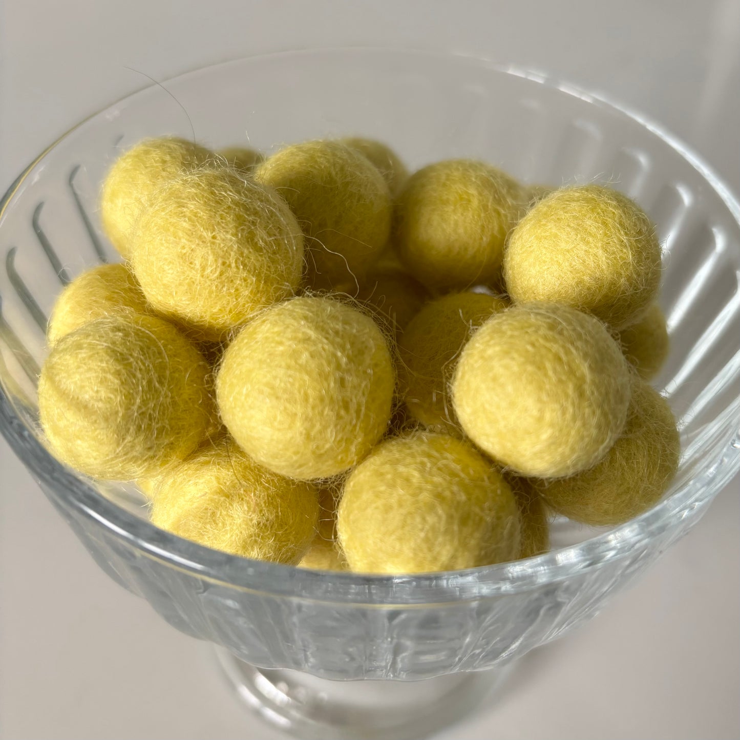 Clear glass bowl filled with yellow felt balls on a white background