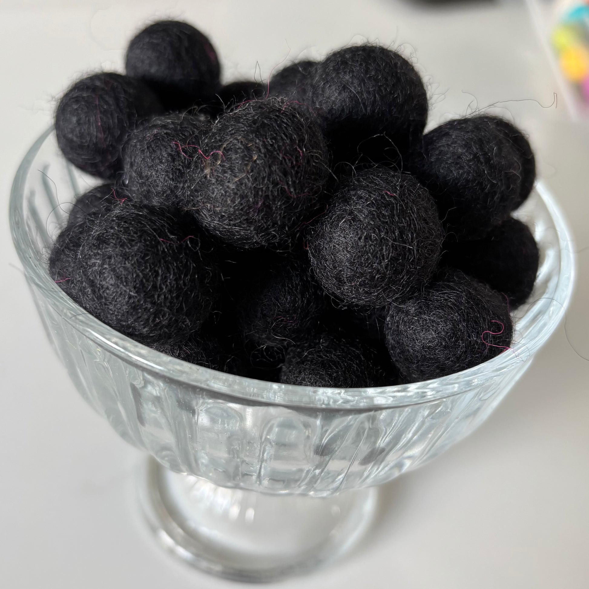 Black felt balls in a glass bowl on a white background
