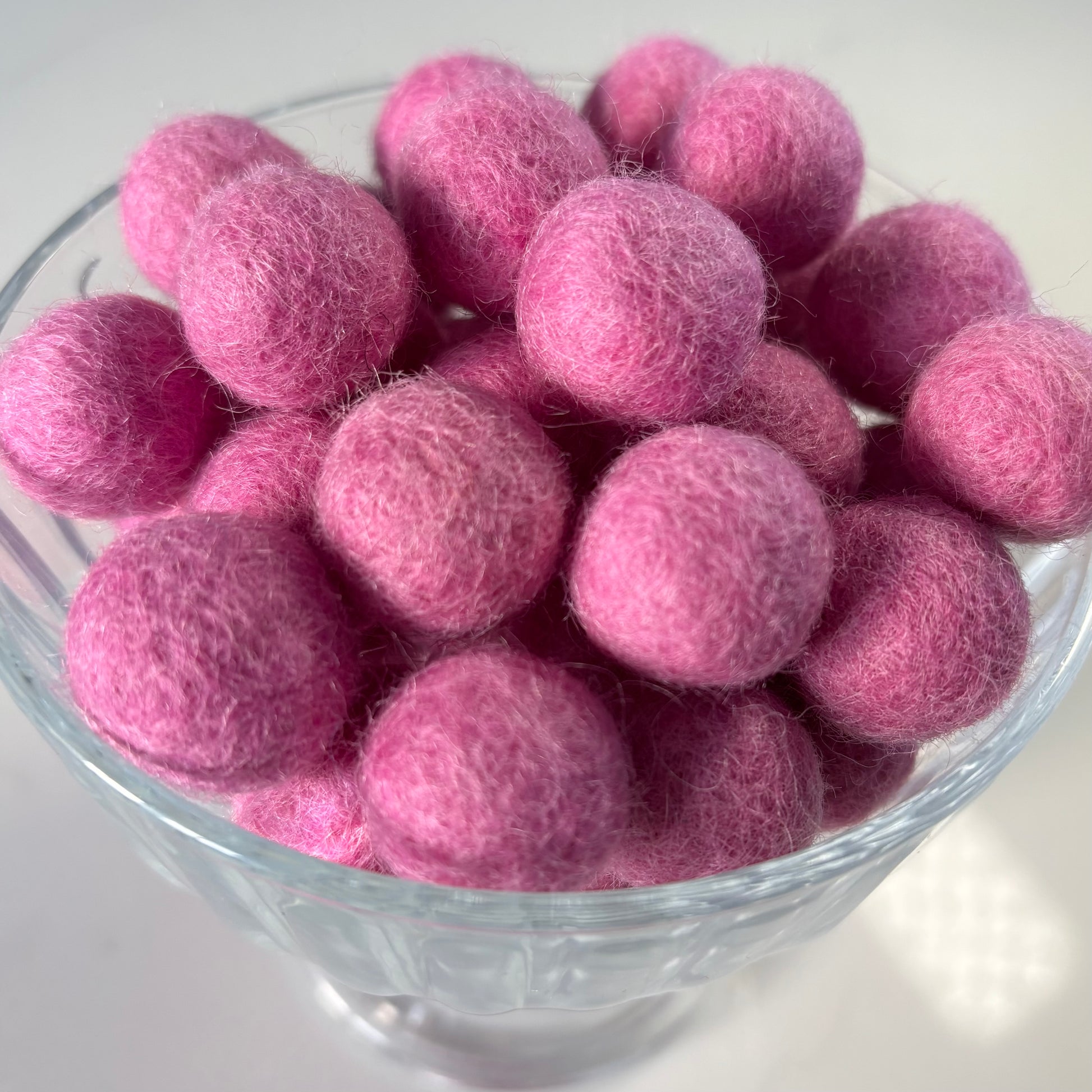 Glass bowl with pink felt balls on a white background