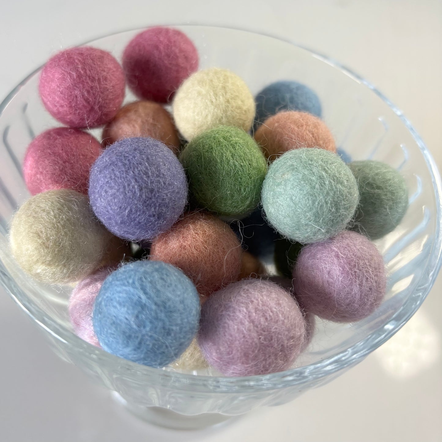Glass bowl filled with multicolored felt balls on a white background