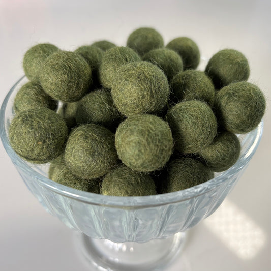 Olive green felt balls in a glass bowl on a white background