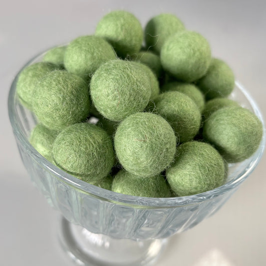 Green felt balls in a glass bowl on a white background