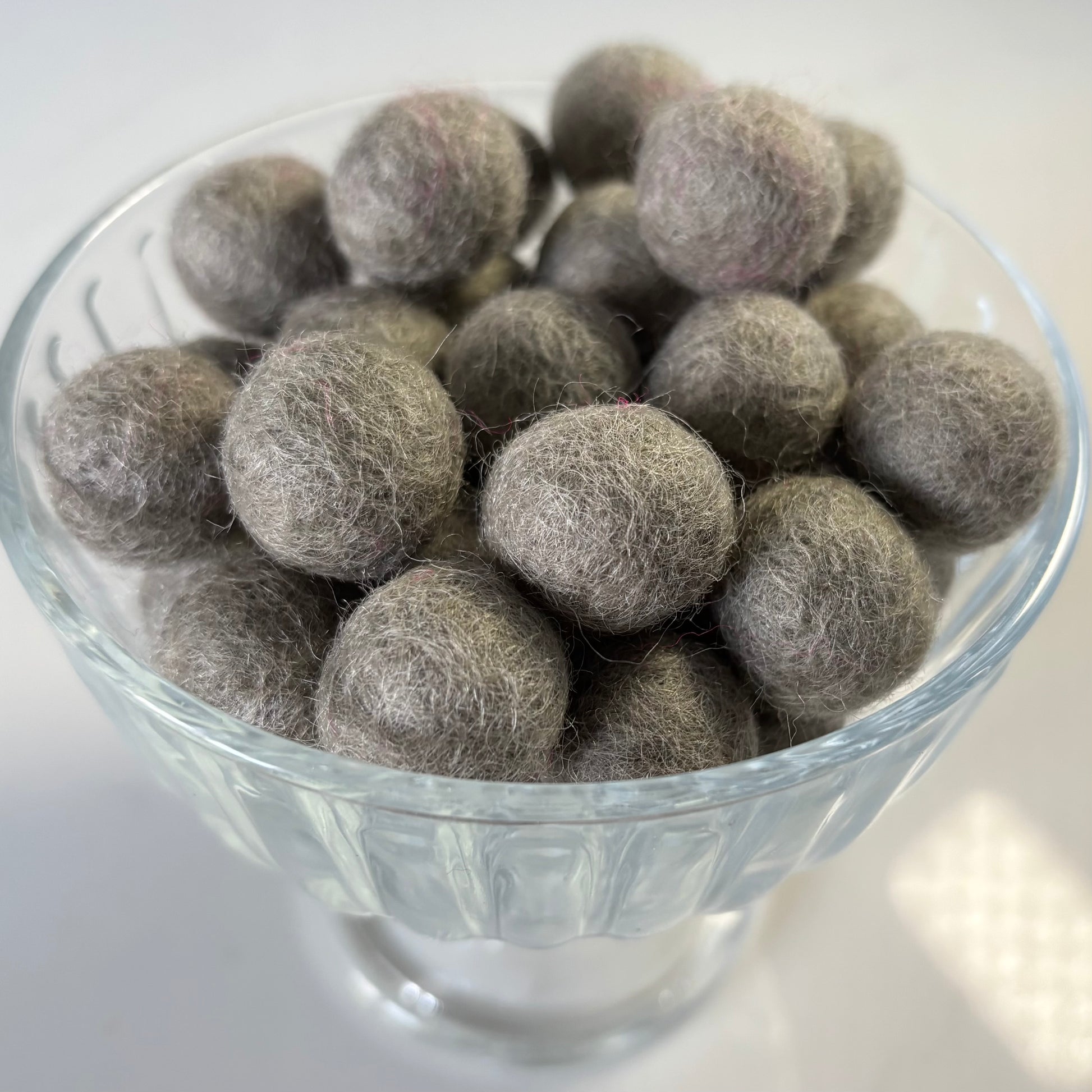 Gray felt balls in a clear glass bowl on a white background