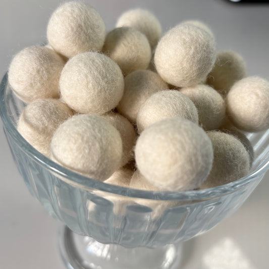 White wool felt balls in a glass bowl on a light background