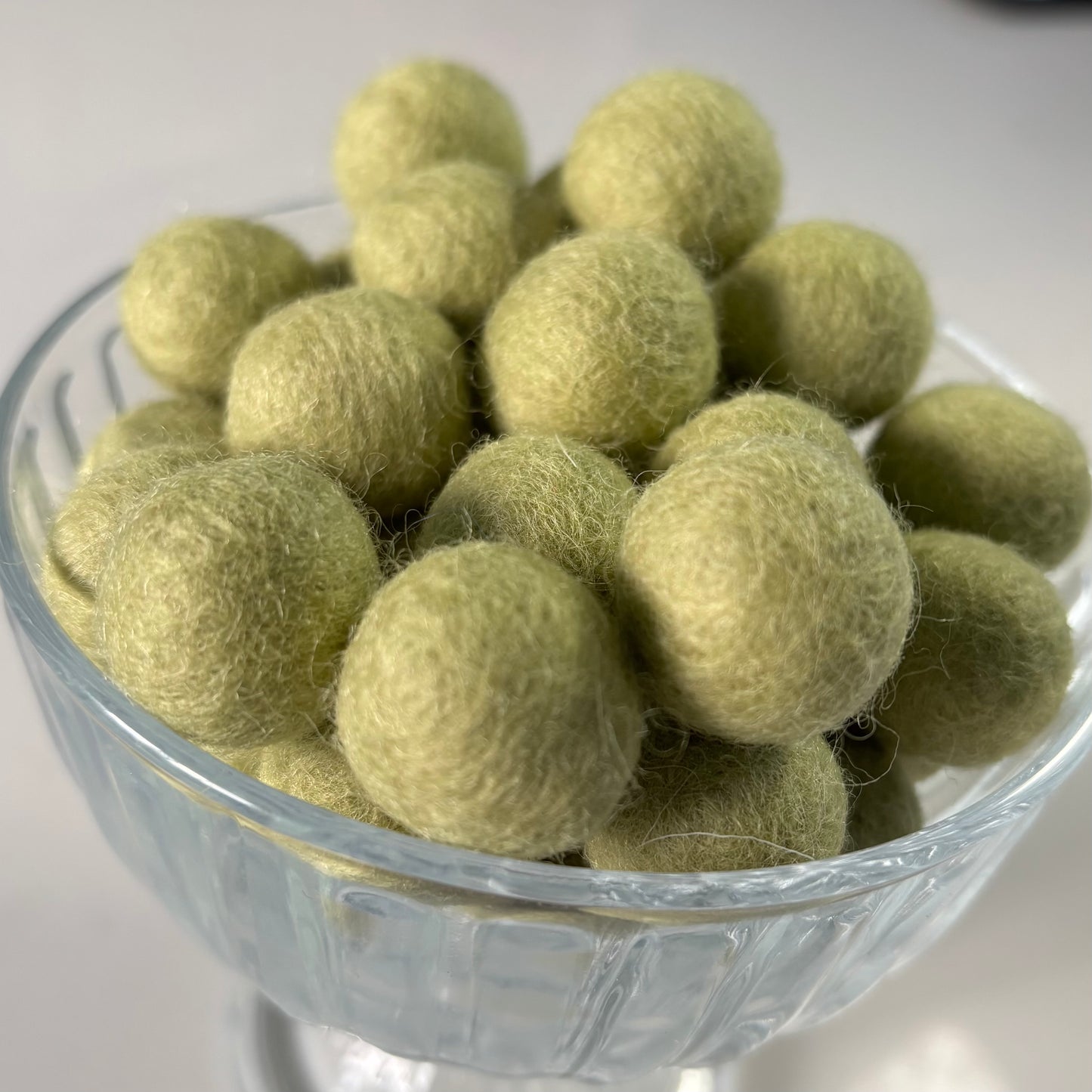 Glass bowl filled with light green felt balls on a white background