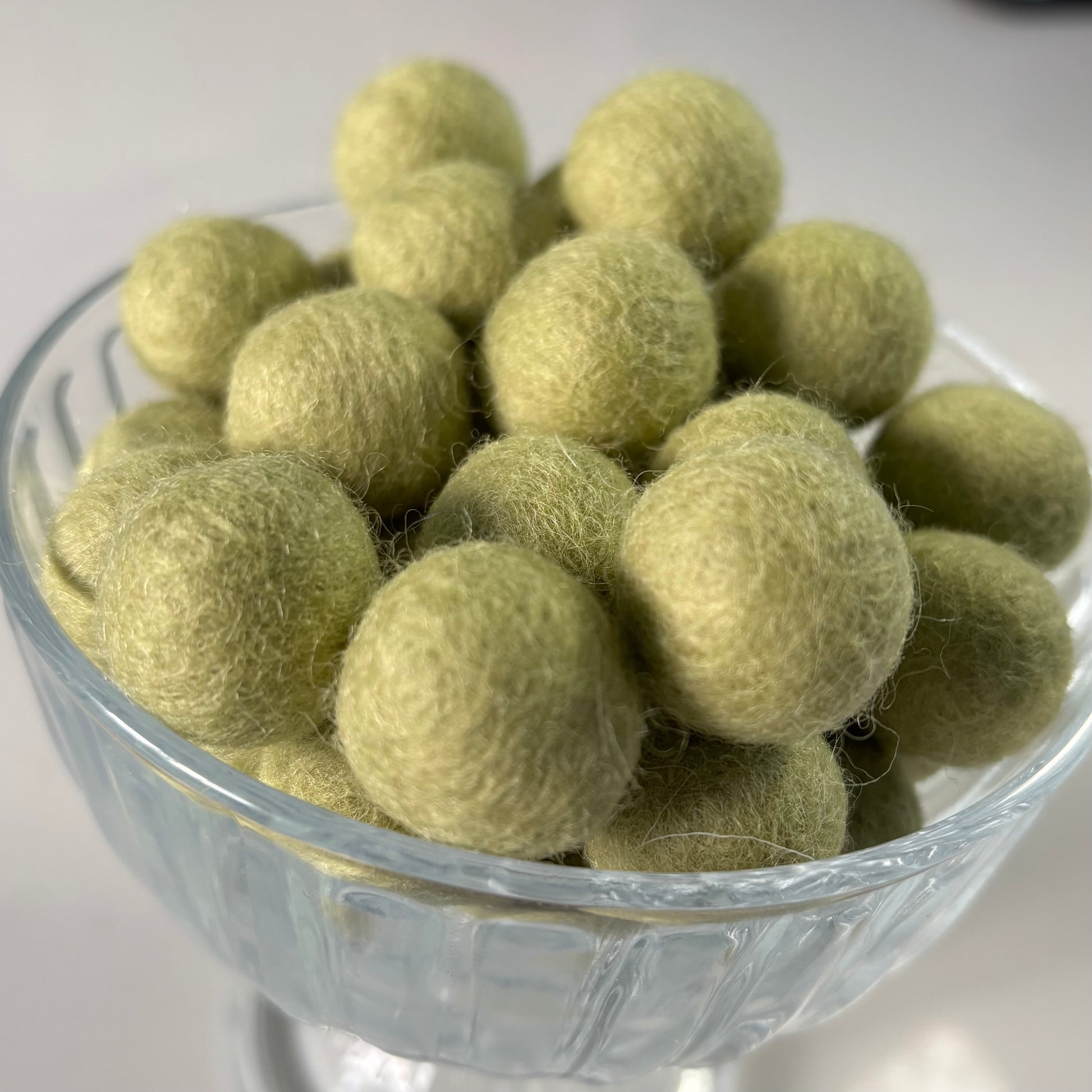 Glass bowl filled with light green felt balls on a white background