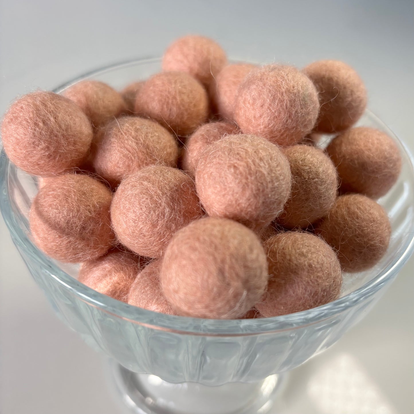 Clear glass bowl filled with peach felt balls on a white background