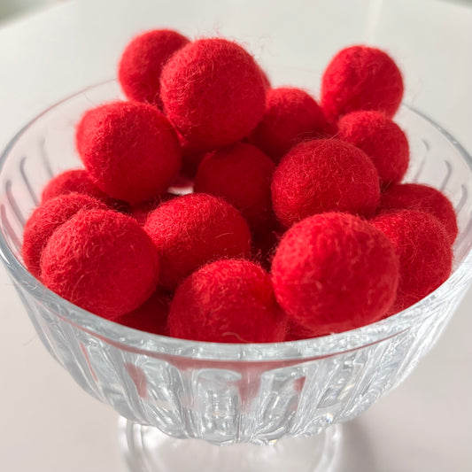 Clear glass bowl filled with red felt balls on a white background