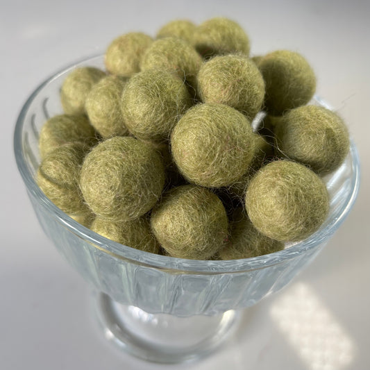 Glass bowl filled with light green felt balls on a white background