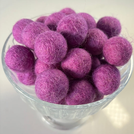 Purple felt balls in a glass bowl on a white background