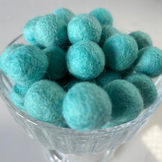 Turquoise felt balls in a glass bowl on a white background